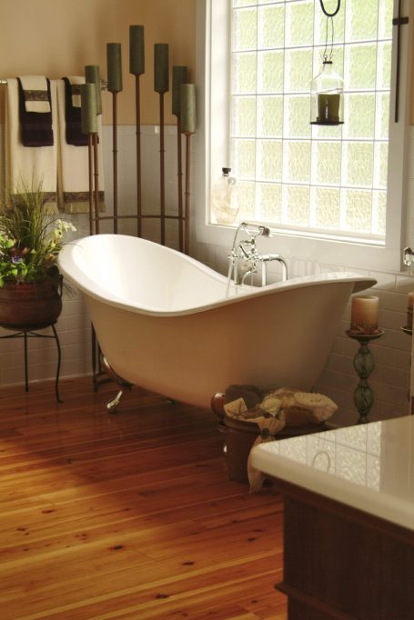 A stylish freestanding bathtub in a bright, warmly lit bathroom setting.