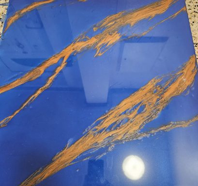 A glossy blue surface with golden streaks and a bright circular reflection.