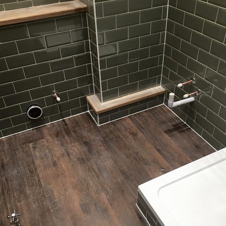 Bathroom with green tiled walls, wooden flooring, and a white bathtub.