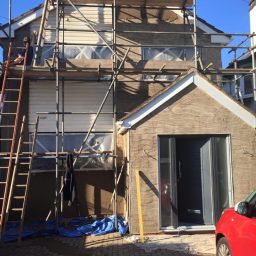 House under renovation with scaffolding, ladder, and a red car parked nearby. Sand and cement finish using a scratch coat and floated top.