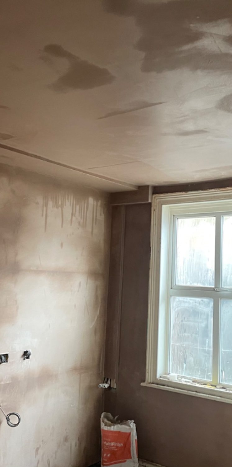 Ceiling and wall with light plastering, window in the background.