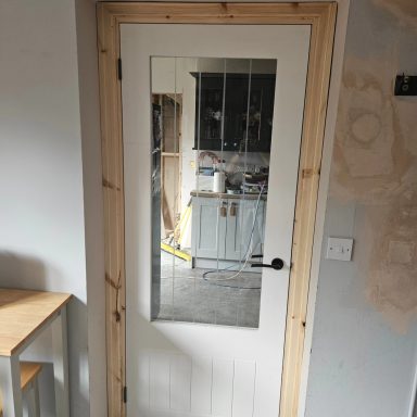 White door with a glass panel framed in wood, leading to a room with furniture.